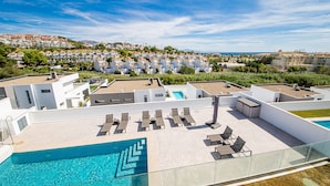 Uma área de piscina no terraço com espreguiçadeiras e piscina, cercada por edifícios modernos e vista para uma cidade costeira.