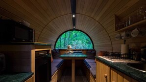 A compact kitchen with a central island, wooden cabinetry, and a view through a large arched window. - Sleep in the Trees - Hot Tub, Sauna and Slide (Chorleywood)