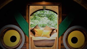 A room with a bed, pillows, and a window with a view of trees. - Sleep in the Trees - Hot Tub, Sauna and Slide (Chorleywood)