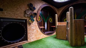 A playroom with circular wooden structures, a large circular window, and a green carpet. - Sleep in the Trees - Hot Tub, Sauna and Slide (Chorleywood)