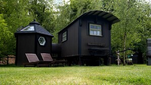 A rustic wooden cabin with a hexagonal window and a small attached structure with benches. - Shepard hut - Hot Tub, Outdoor Shower, Bath (Chorleywood)