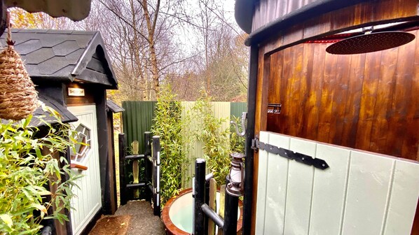 A rustic wooden door with a metal latch, a small outdoor toilet with a black seat, and a green fence in the background.