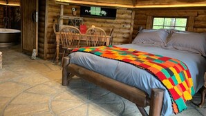 A cozy log cabin bedroom with a bed, a wooden chair, a small table, and a mounted television. - Hagrid Hut Themed - Hot Tub - Warner Bro Studio (Chorleywood)