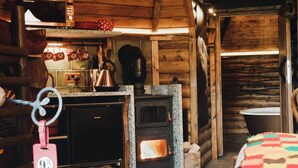A cozy cabin interior with a wood-burning stove, a microwave, and a kettle on the countertop. - Hagrid Hut Themed - Hot Tub - Warner Bro Studio (Chorleywood)