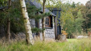 A rustic stone cabin with a wooden window, surrounded by trees and autumn foliage. - Hagrid Hut Themed - Hot Tub - Warner Bro Studio (Chorleywood)
