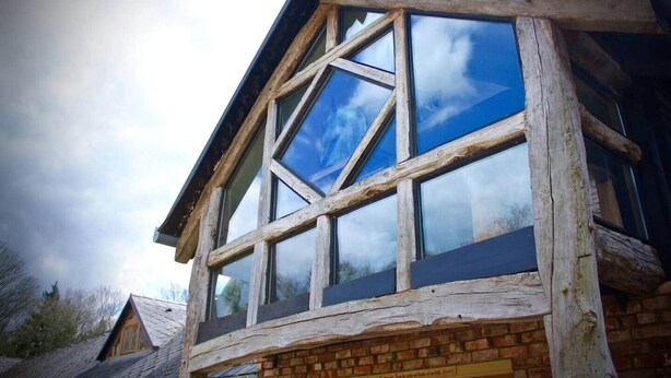 A building with a large, multi-pane window structure and a brick base. - Hagrid Hut Themed - Hot Tub - Warner Bro Studio (Chorleywood)
