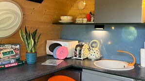 A compact kitchen with wooden ceiling, a microwave, a toaster, a sink, and two orange stools. - Dinky Disc - Cosy Hot Tub Escape (Chorleywood)