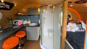 A compact, well-lit room with a kitchenette, a shower, and a bed with a unique circular design. - Dinky Disc - Cosy Hot Tub Escape (Chorleywood)