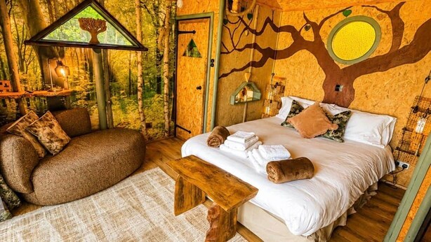 A cozy bedroom with a bed, a bench, and a small table. - Tree House - Hot Tub on balcony (Chorleywood)