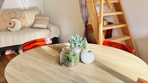 A round wooden table with a glass top, surrounded by red chairs, in a room with a wooden staircase and a sofa with cushions. - Bright little studio near Porto Vecchio🌴 (San-Gavino-di-Carbini)