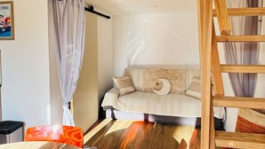 A room with a wooden ceiling, a sofa with patterned cushions, a wooden ladder, and a window with curtains. - Bright little studio near Porto Vecchio🌴 (San-Gavino-di-Carbini)