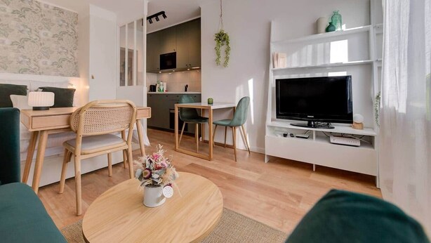 Een moderne woonkamer met een bank, een eettafel, stoelen, een televisie en een keuken op de achtergrond.