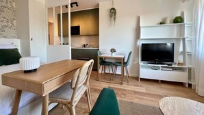 Een moderne hotelkamer met een houten eettafel, een televisie en een kitchenette op de achtergrond.