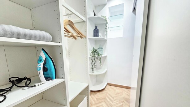 Un espace de rangement moderne et bien aménagé, doté d’étagères, d’un portant et d’un fer à repasser visible.