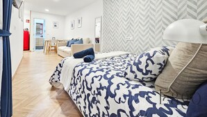 Une chambre d’hôtel moderne avec un grand lit, un bureau et, au fond, une petite cuisine.