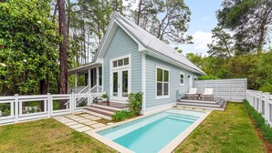 Ein hellblaues Haus mit Swimmingpool, weißem Zaun und einer Veranda mit Gartenmöbeln.
