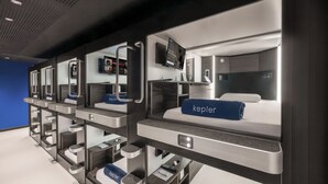 Een rij moderne, compacte hotelkamers met aparte bedden, ingebouwde televisies en persoonlijke opbergruimtes.