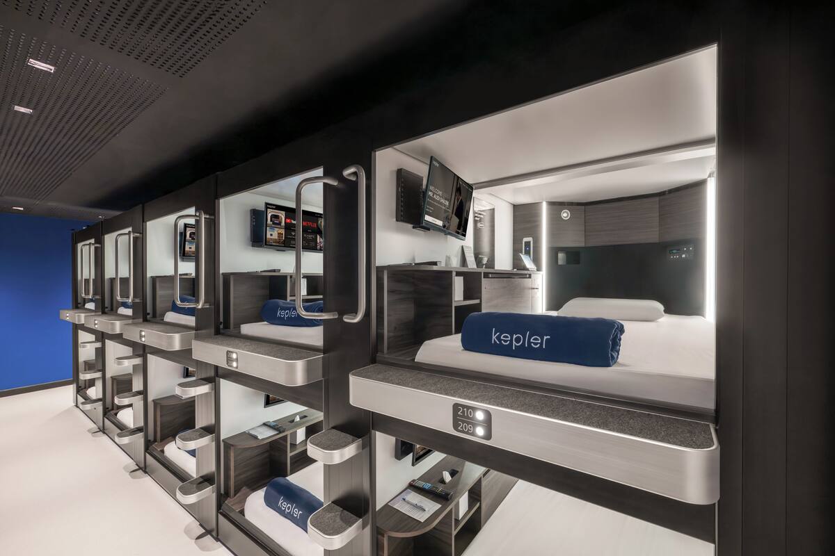 Une rangée de chambres d’hôtel modernes et compactes, dotées de lits individuels, de téléviseurs intégrés et d’espaces de rangement personnels.