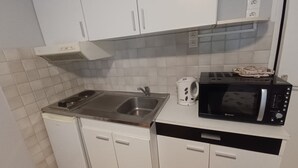 Ett kompakt kök med vita skåp, en diskho i rostfritt stål, en svart mikrovågsugn och en vattenkokare.