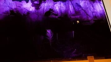 Une vue nocturne d’une montagne illuminée de lumière violette, avec une enseigne indiquant « TRIPORT-TERRASSE », et un arbre au premier plan.