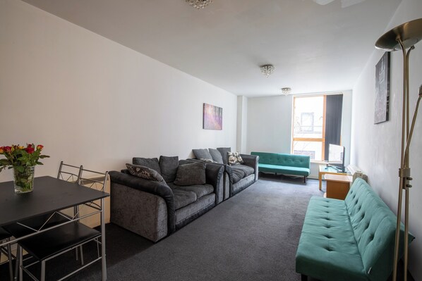 A living room with a sofa, a green couch, a dining table, and a floor lamp. - Manchester High St (Manchester)