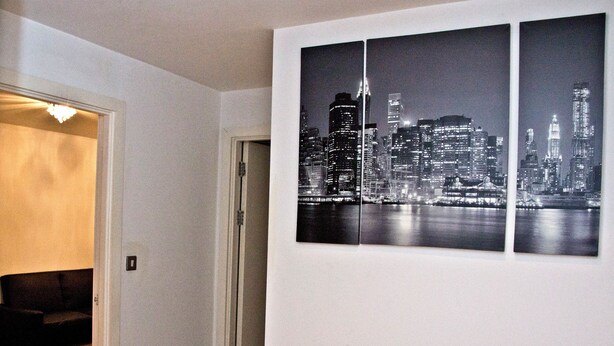 Um corredor com uma porta que dá para um quarto. Há três fotografias a preto e branco de um horizonte urbano na parede.