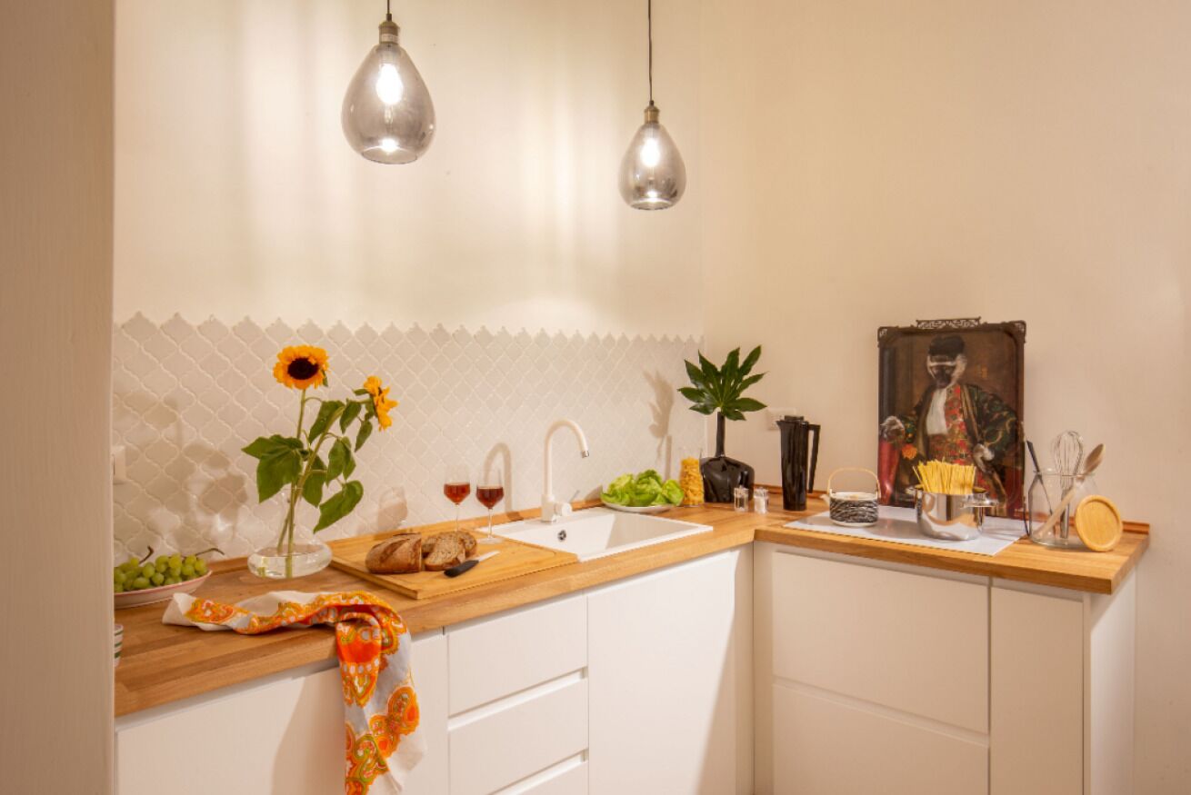 A kitchen with a wooden countertop, white cabinets, a sink, and hanging pendant lights.