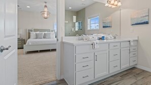 A modern bathroom with a large mirror, white cabinetry, and a chandelier. - Gone Gulfing - Isle Be Chillin (Pensacola)