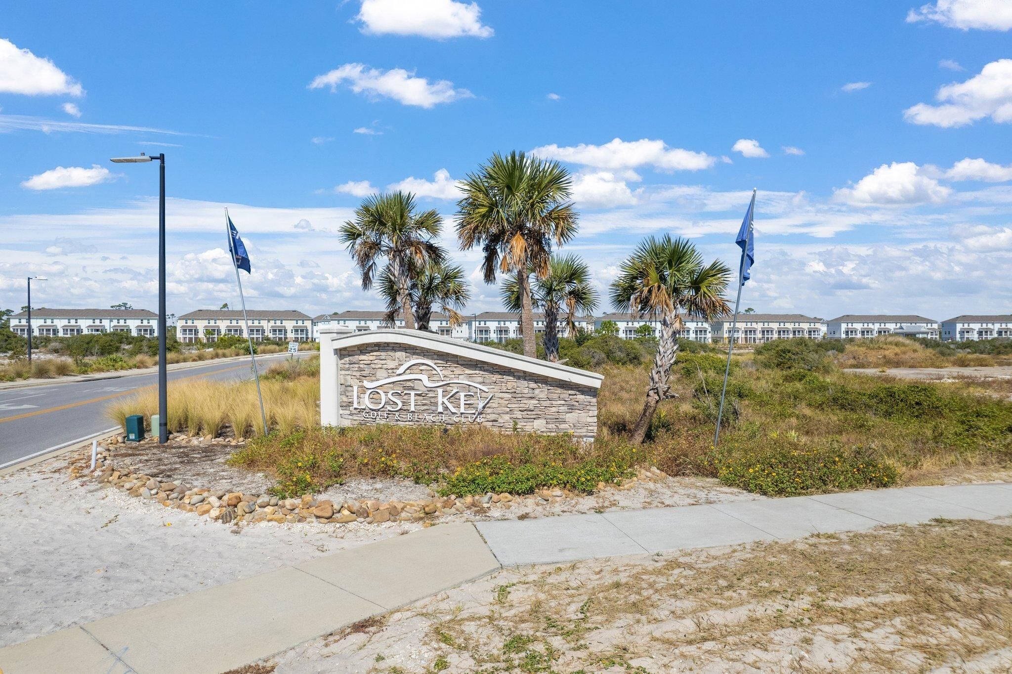 A hotel entrance with a stone sign, palm trees, and a clear sky.