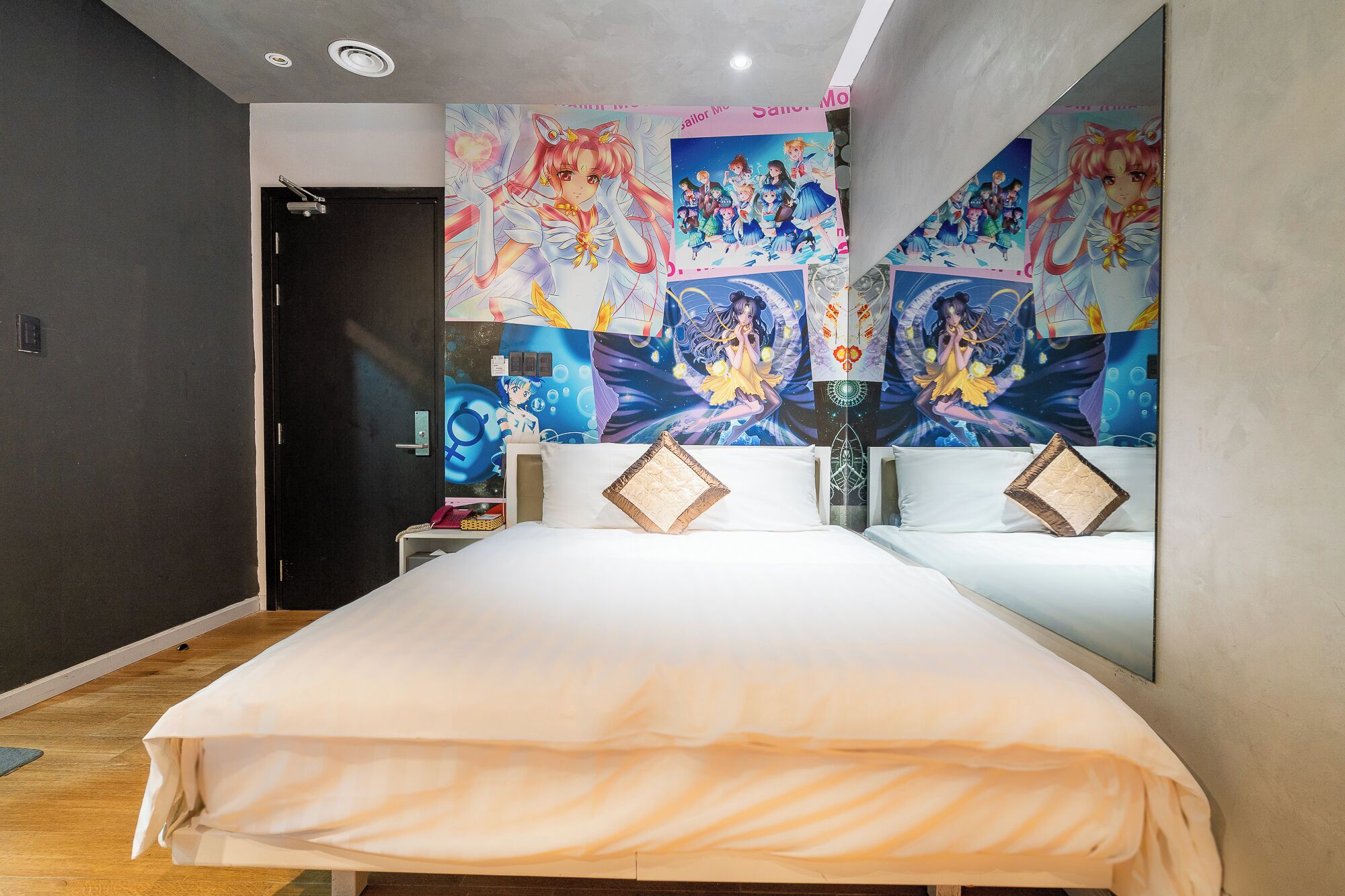 Una habitación de hotel con una cama grande, dos almohadas, una mesita de noche y una pared decorada con carteles de anime.