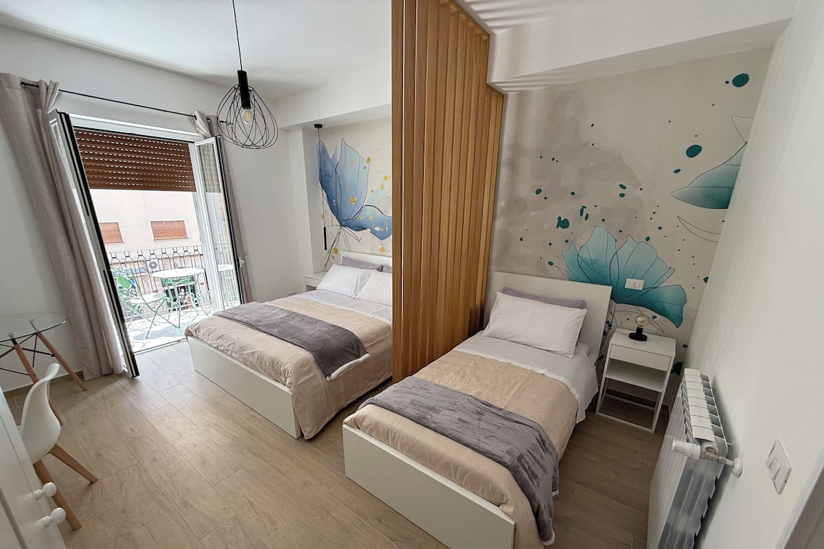 Une chambre moderne avec deux lits, un balcon et une fresque murale décorative.