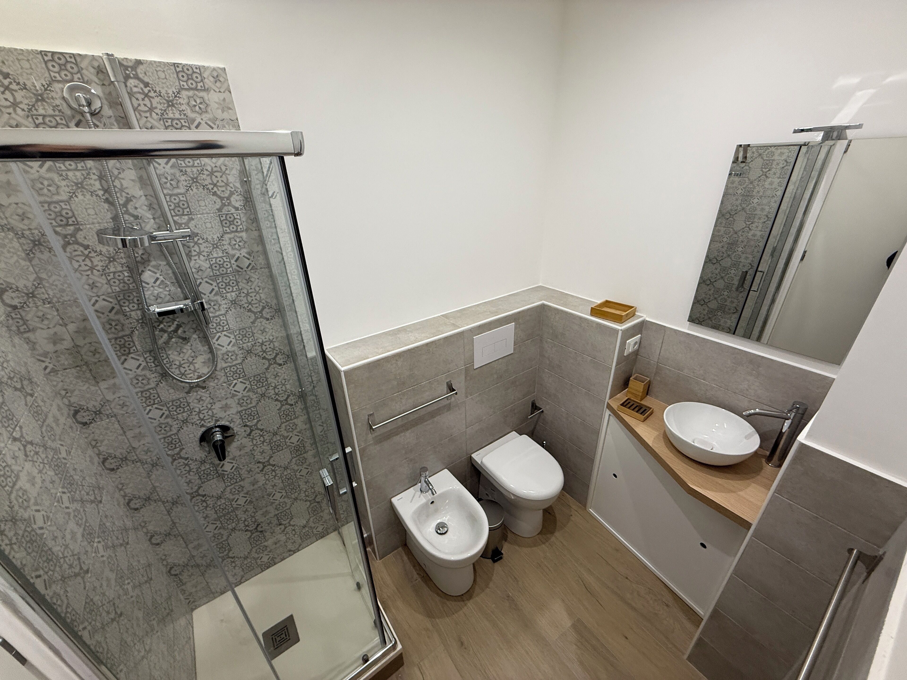 Une salle de bain moderne dotée d’une douche à parois de verre, d’un bidet et d’un lavabo avec un plan de travail en bois.