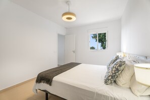 A bedroom with a bed, bedside table, lamp, and a window with a view of trees. - Vacation Apartment 'Beautiful Sea View and Pool Finca 6' with Sea View, Shared Pool and Wi-Fi (Adeje)