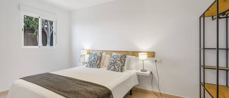 A bedroom with a bed, bedside lamps, a window, and a wooden shelf unit.