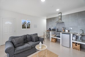 A modern kitchen with a built-in microwave, stove, and sink. There is a grey sofa and a small round table with a decorative item. - Vacation Apartment 'Beautiful Sea View and Pool Finca 6' with Sea View, Shared Pool and Wi-Fi (Adeje)