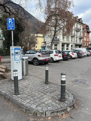 A parking area with a payment kiosk, bollards, and a sign for a central parking area. - Pearl Apartment (Interlaken)