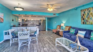 A spacious living area with a blue wall, a dining table with chairs, a blue sofa with cushions, and a ceiling fan. - Holiday Villas III #209 (Indian Shores)