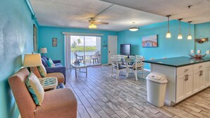 A bright room with teal walls, a wooden floor, a ceiling fan, a dining table with chairs, a sofa, and a TV. - Holiday Villas III #209 (Indian Shores)
