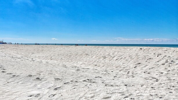 A wide sandy beach with footprints leading to the water, a clear blue sky, and a distant horizon. - Holiday Villas III #209 (Indian Shores)