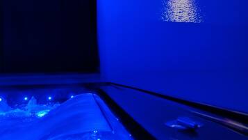 A room with a television displaying a sunset over water, a bed with a blue light under it, and a window with a view of mountains.