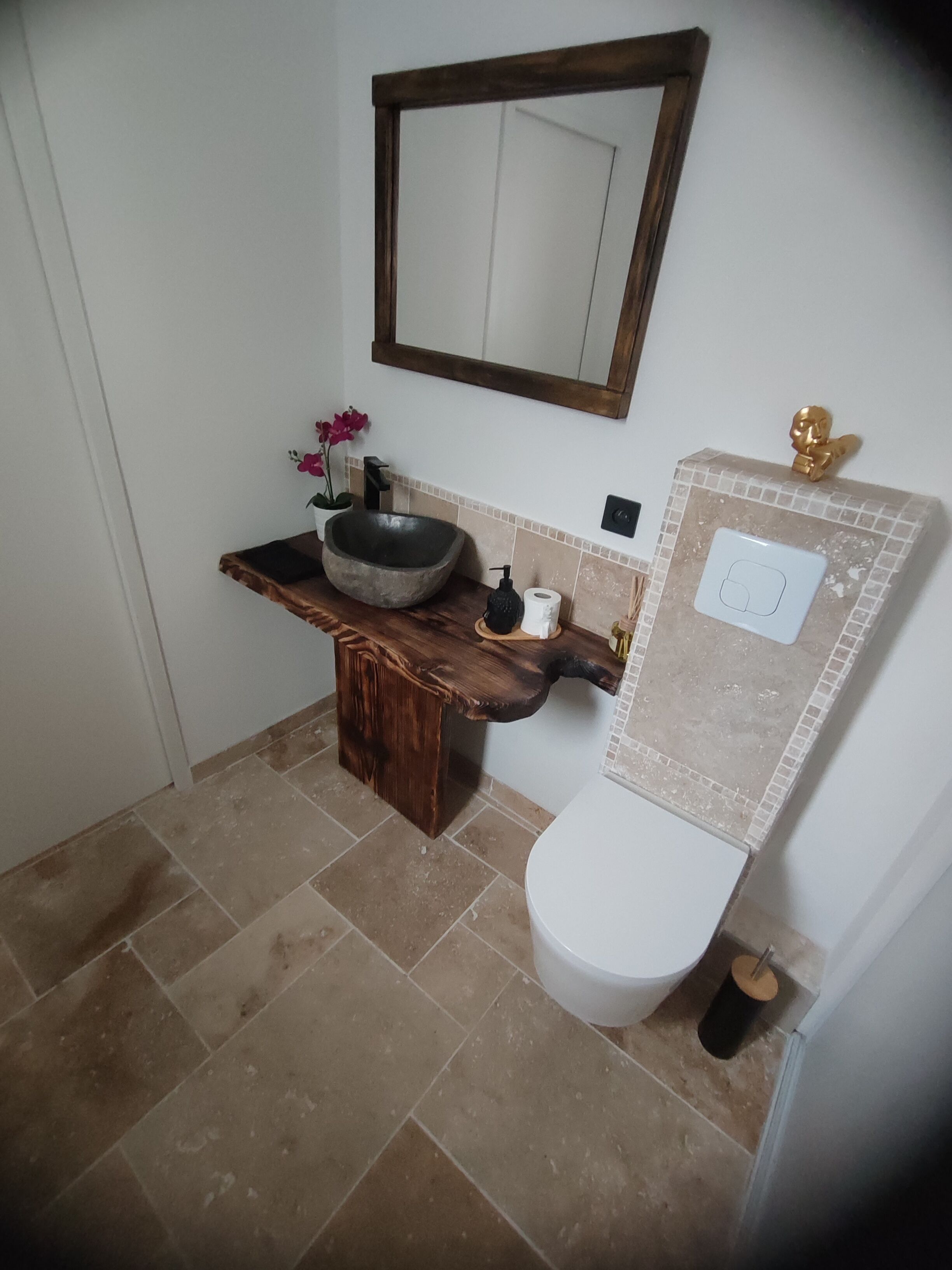 A bathroom with a wooden vanity, a stone sink, a mirror, and a toilet.
