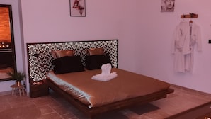 Quarto moderno com cama grande, cabeceira com design perfurado, mesa de cabeceira pequena com uma planta e um porta-roupas fixado na parede.