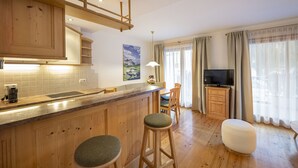 A kitchen with wooden cabinets, a bar area with stools, a dining table, and a TV. - 1010A Marienstern Apartments (Santa Cristina Valgardena)