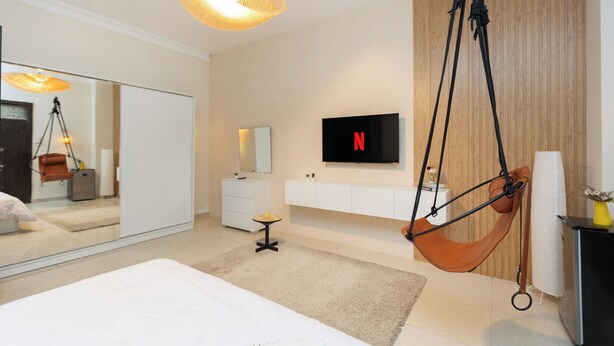Een moderne slaapkamer met een hangstoel, een grote spiegel, een televisie en een minimalistisch design.