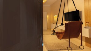 Een kamer met een hangstoel, een aan de muur bevestigde televisie en een deur.