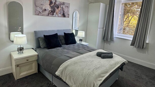 A modern bedroom with a bed, bedside lamps, a large mirror, and a window with curtains. - Sleeps4- Sofabed- 5mintocitycentre- Glasgowgreen (Glasgow)