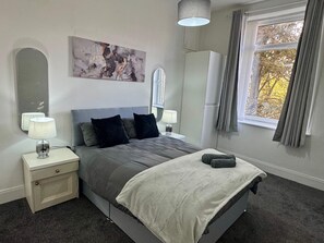 Een moderne slaapkamer met een bed, nachtlampjes, een grote spiegel en een raam met gordijnen.