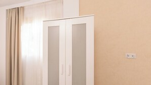 Ein Zimmer mit Schrank, Steckdose an der Wand und einem Vorhangfenster.