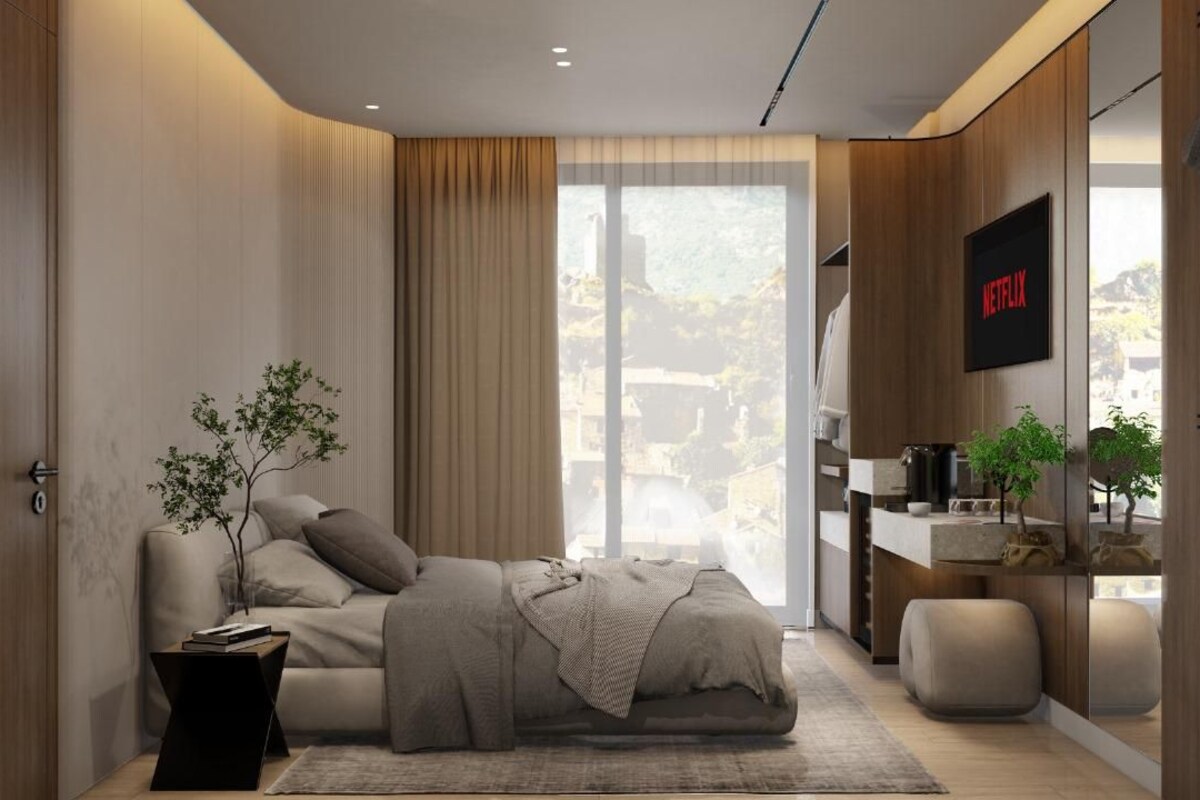 A modern bedroom with a bed, a side table, a TV, and a view of the outdoors.