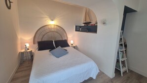 A bedroom with a bed, two bedside lamps, a small shelf with a sailboat model, and a ladder with books.